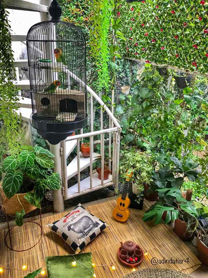 Cozy veranda space filled with lush green plants, small birdcage, farmhouse cushion, and bamboo mat flooring