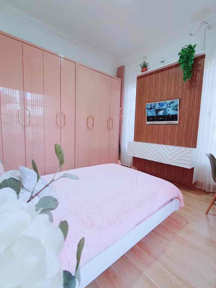 Cozy bedroom with pink wardrobe and bedding, wood tone flooring and TV stand arranged neatly