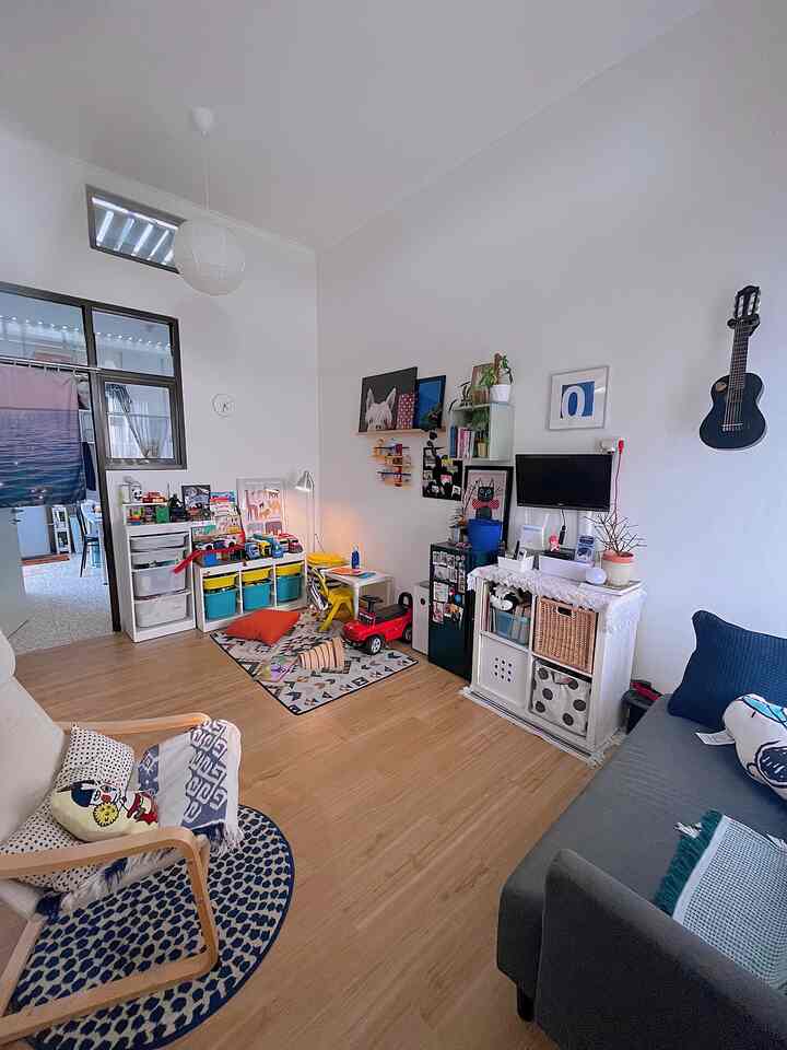 Bright white walls and wood-tone flooring define a living room and kids' play area featuring shelves, sofa, and armchair in a cozy setting