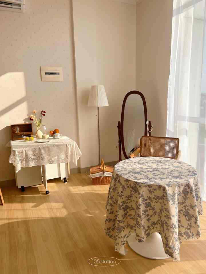 Warm natural color studio apartment featuring a round floral tablecloth-covered table, rattan chair, and vintage Korean style interior