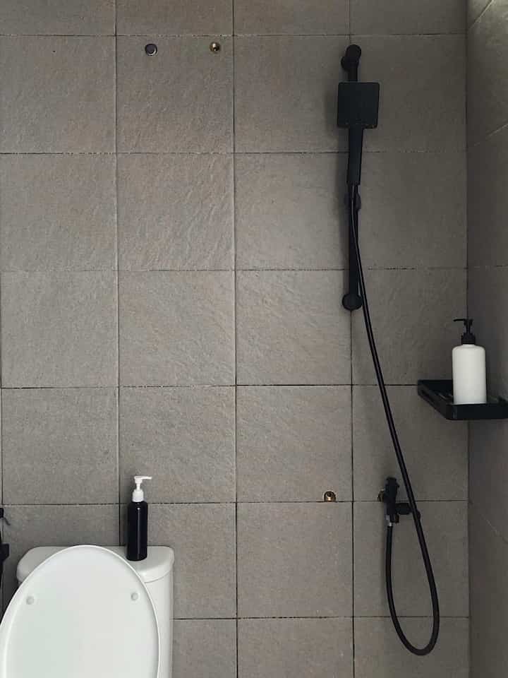 Gray monotone tiled bathroom featuring a black showerhead and corner storage in a compact space