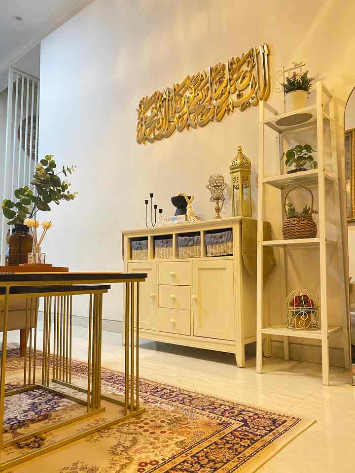 White and gold toned living room featuring a storage cabinet, shelving unit, golden wall art, and patterned rug with cozy atmosphere