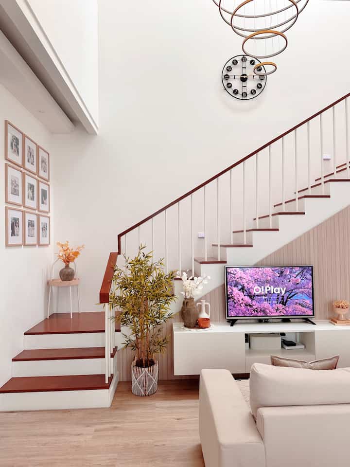 White and brown tone living room featuring sofa, large plant, and TV under staircase with a simple modern atmosphere