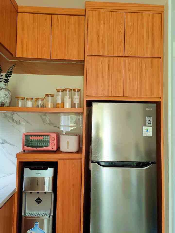 Warm brown-toned kitchen featuring neat wooden cabinets, stainless steel refrigerator, and an automatic rice bucket with a clean atmosphere