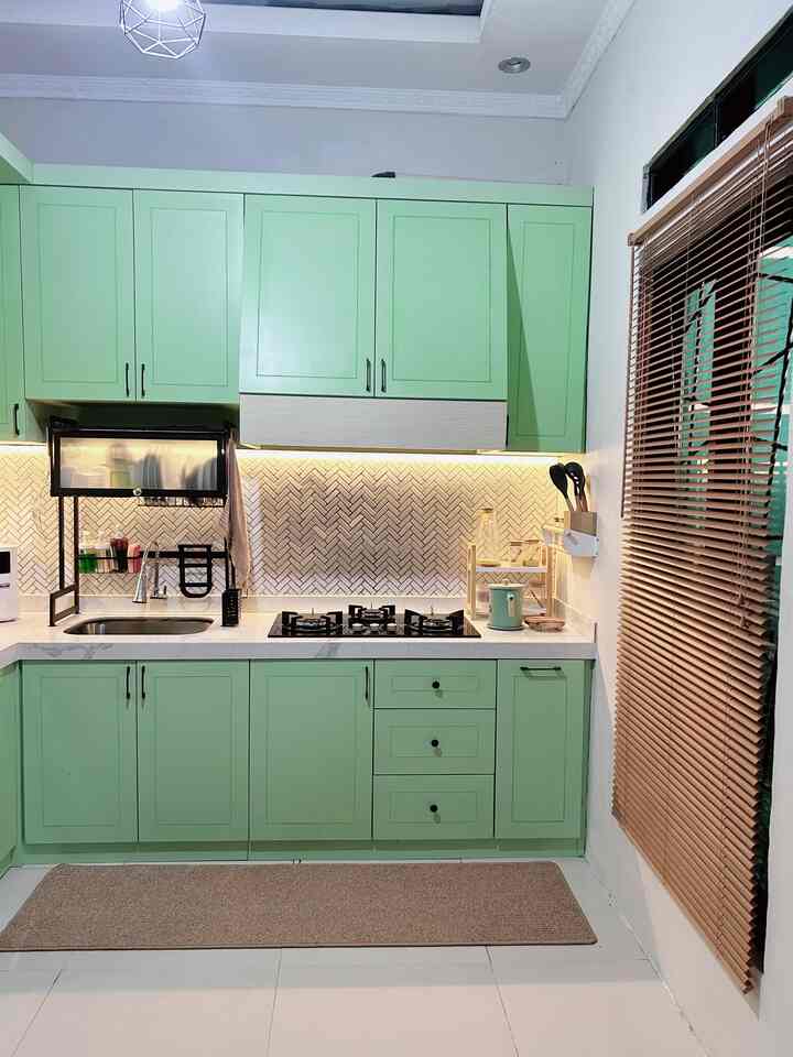 A clean kitchen space featuring light green cabinets and wooden venetian blinds with neutral tones