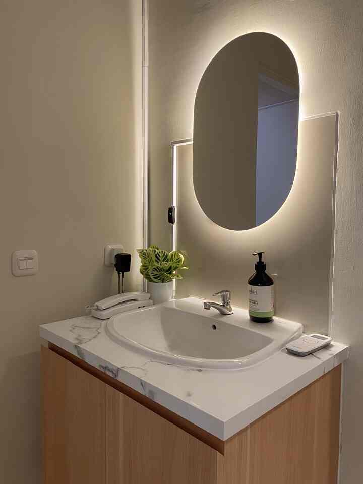 White-toned bathroom featuring a natural wood cabinet with a marble countertop sink and an LED illuminated oval mirror