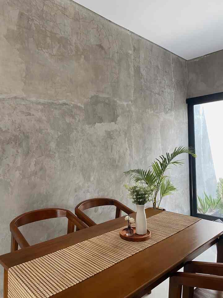 Compact two-person dining room with gray concrete walls and wood-tone dining table, decorated with natural plants for cozy atmosphere