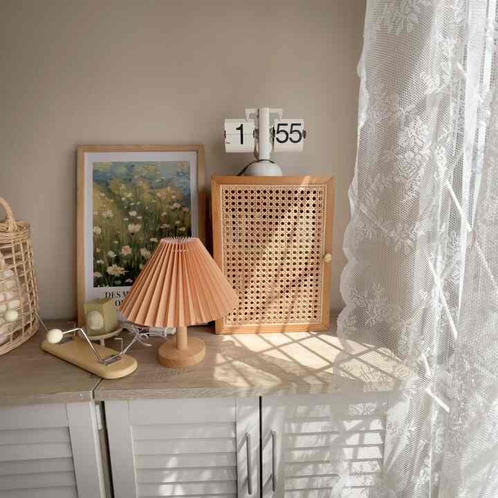 Soft white and wood tone corner storage space featuring a table lamp and picture frame bathed in natural sunlight for cozy atmosphere