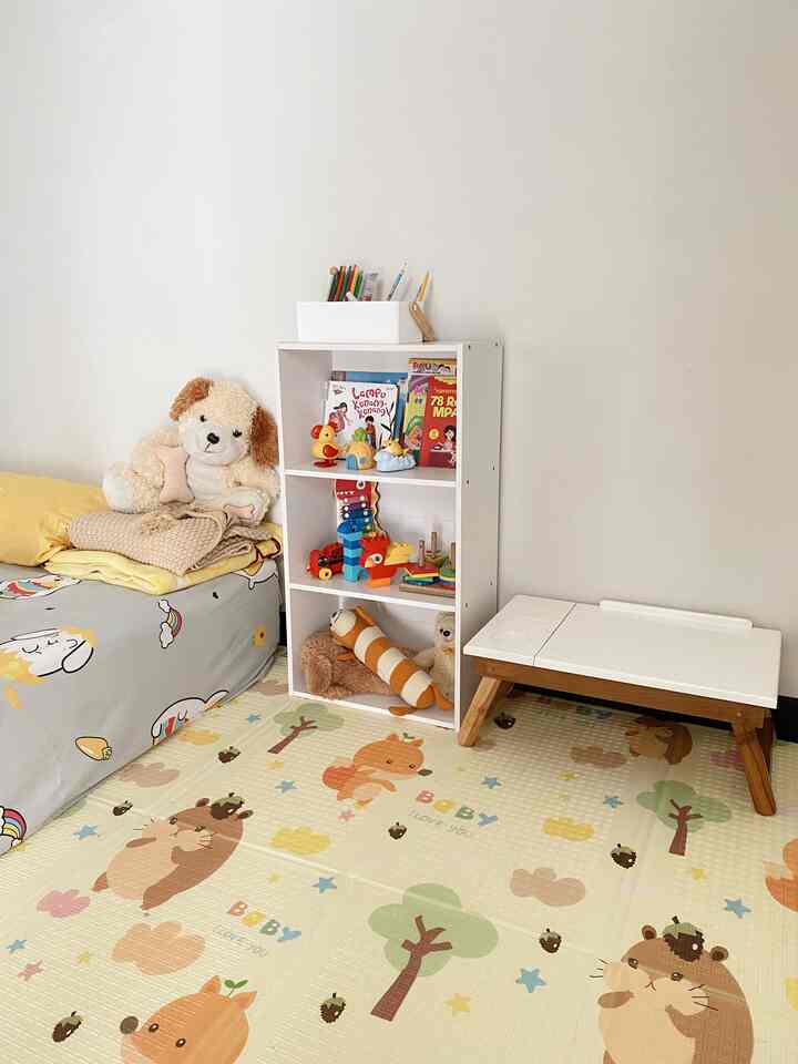 Beige playmat with white bookshelf and yellow bedding in a kids' bedroom space
