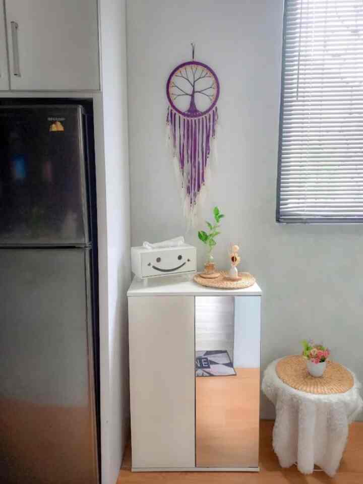 White-toned kitchen-adjacent space featuring shoe cabinet, Venetian blinds, and natural decor accessories in a simple storage setting