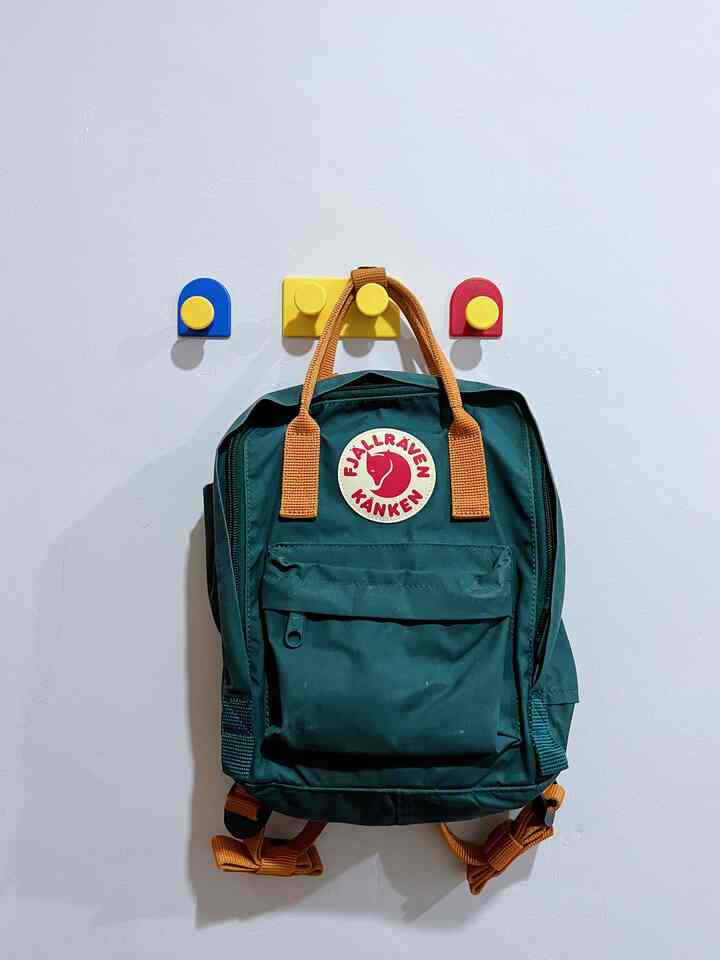 Simple kids' room interior with a green backpack hung on bright white wall featuring colorful hooks