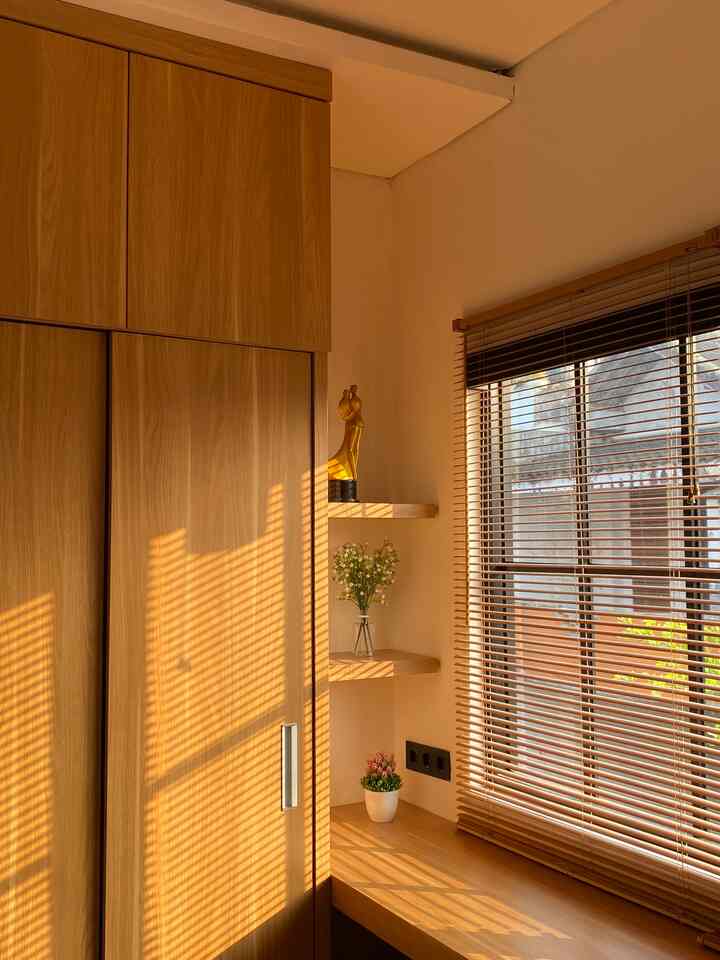 Warm brown wood tone bedroom featuring large wooden wardrobe and Venetian blinds creating a cozy home office vibe