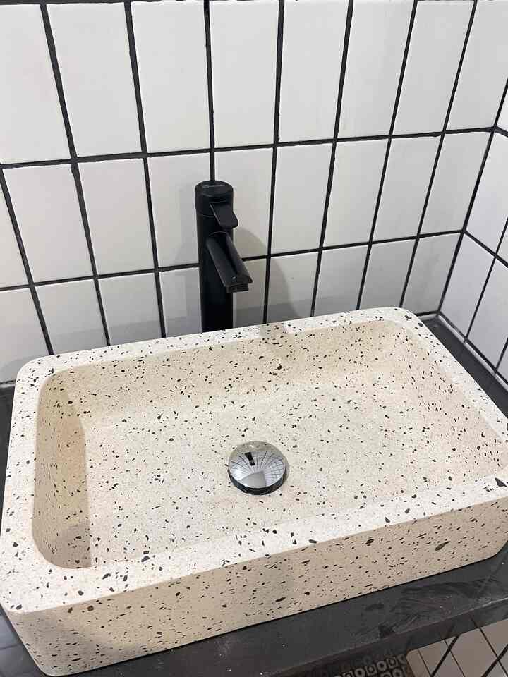 Monotone white tiled wall corner featuring a terrazzo washbasin with black faucet in a simple bathroom