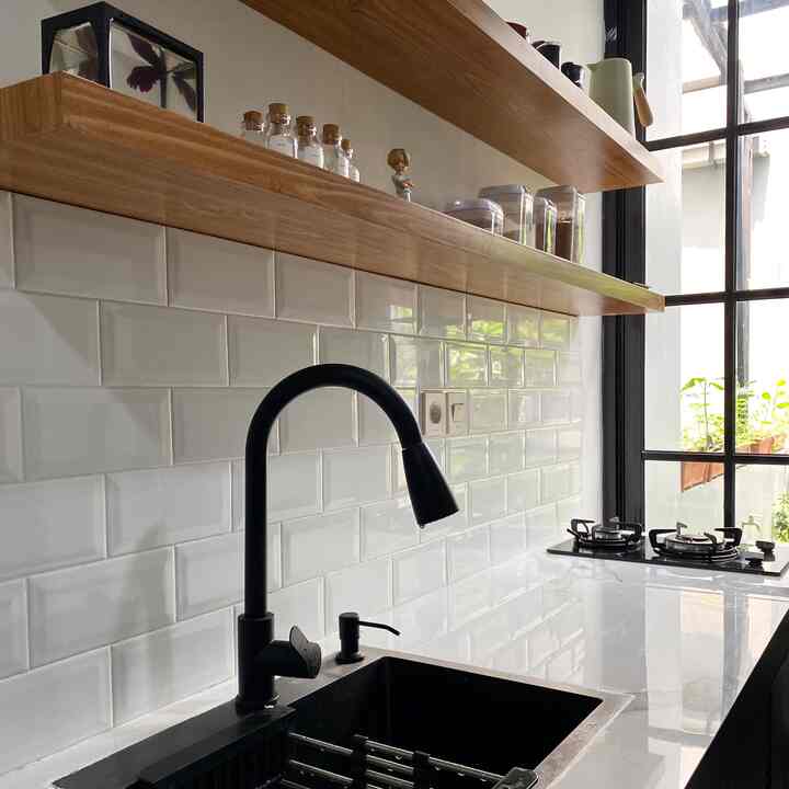 A modern industrial small kitchen with white tiles and wooden shelves, featuring a black sink and compact cooking area