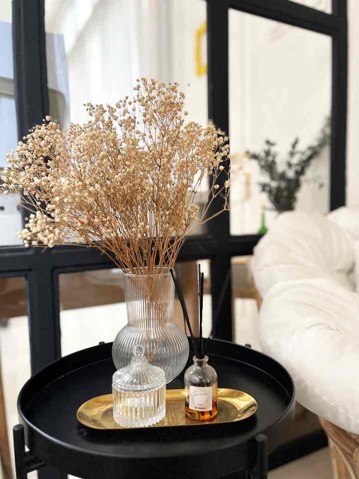 White and natural tone entrance space featuring rattan armchair and console table with diffuser and dried flower decor, simple minimal interior