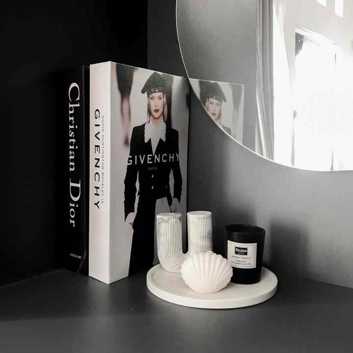 Monotone-toned bookshelf and mirror on a vanity surface featuring decorative objets and a candle in a cozy setting