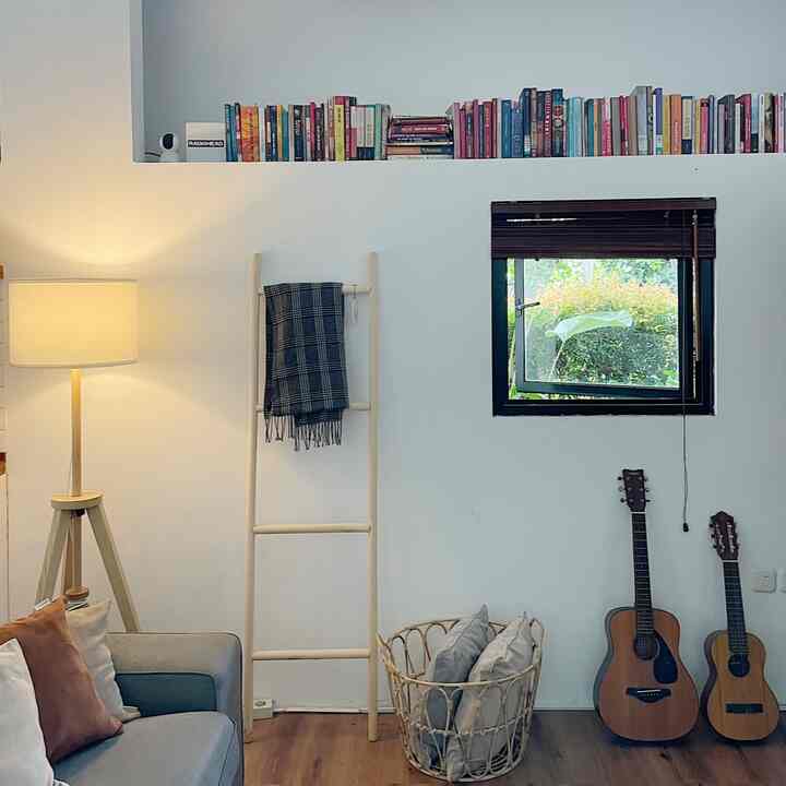 White and brown toned living room featuring sofa, floor lamp, bookshelf, and rattan basket arranged with cozy feel