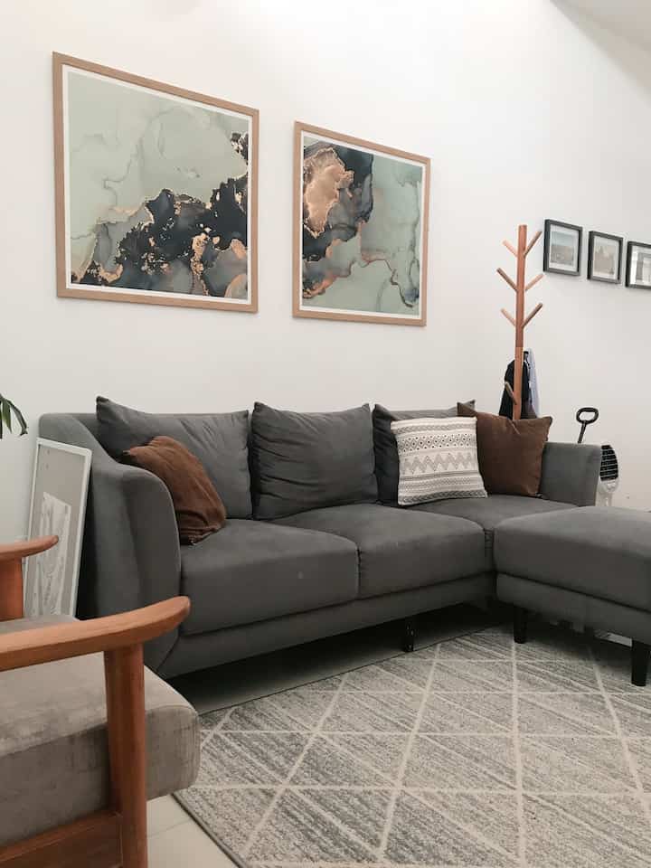 Gray and wood tone living room featuring a gray sectional sofa with cushions and abstract framed wall art creating a cozy atmosphere