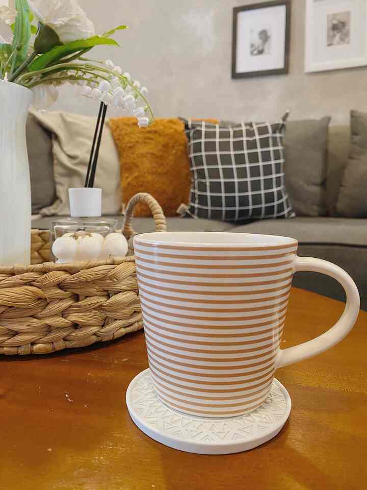Natural-toned living room café space with gray sofa and brown coffee table featuring a striped mug on a white coaster