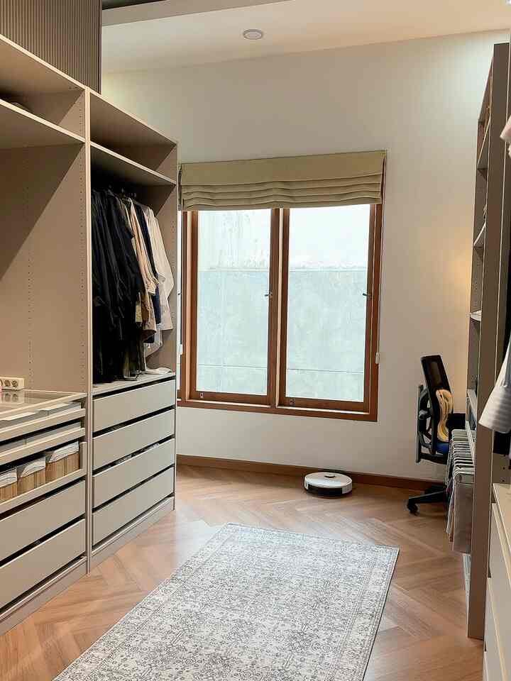 Beige and wood tone walk-in closet featuring wardrobes and a Roman Shade Blind with a warm, organized atmosphere