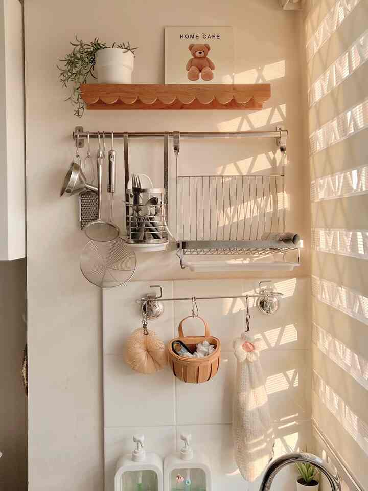 Creamy white-toned small kitchen wall featuring wooden shelf and neatly arranged stainless steel kitchen utensils