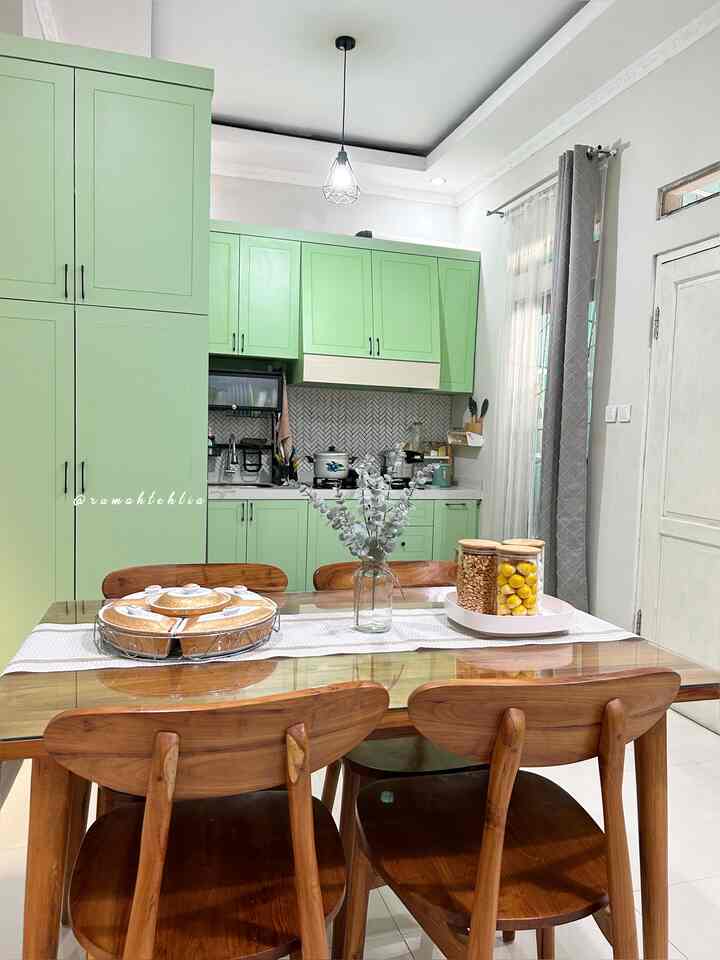 Cozy dining room featuring soft green kitchen cabinets and natural wooden dining table and chairs with warm atmosphere