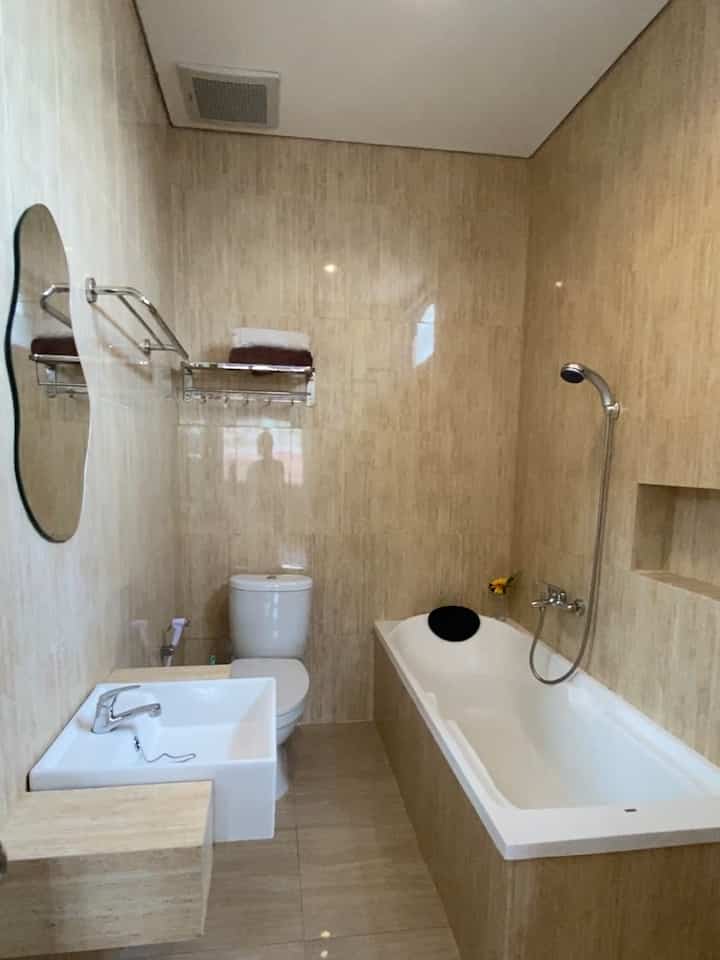 Beige tiled long narrow bathroom featuring white bathtub, sink, and toilet with a natural tone