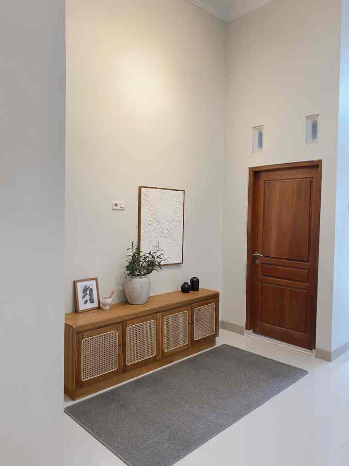 Beige walls and wood tone cabinet arranged in a neat entrance area, with a gray rug placed on the floor