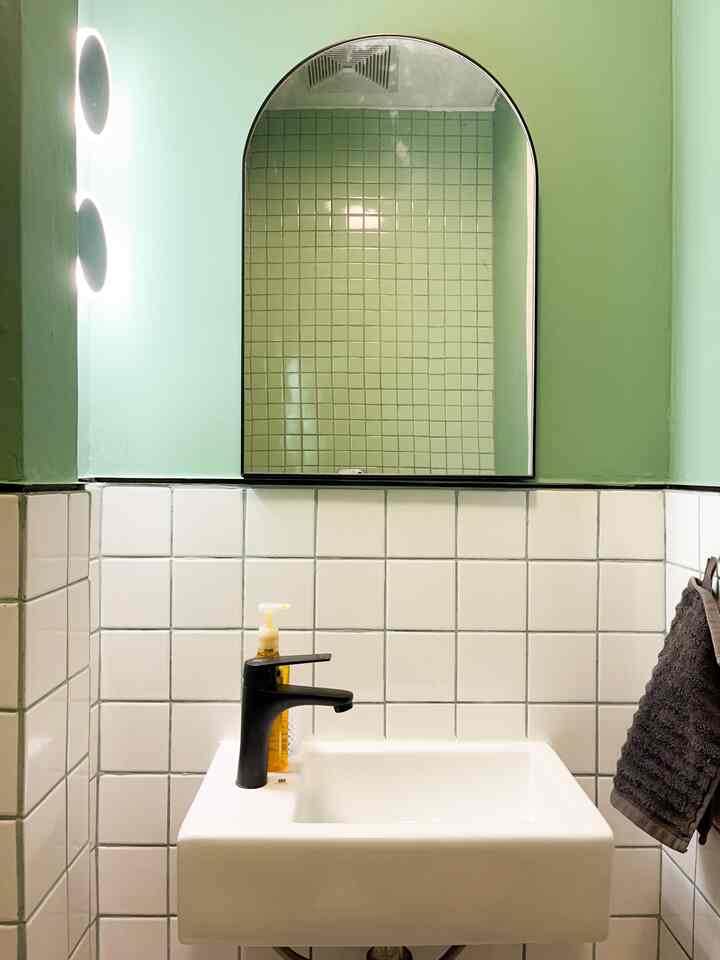 Light green and white tiled compact powder room with black faucet and towel rack, featuring a modern, narrow design