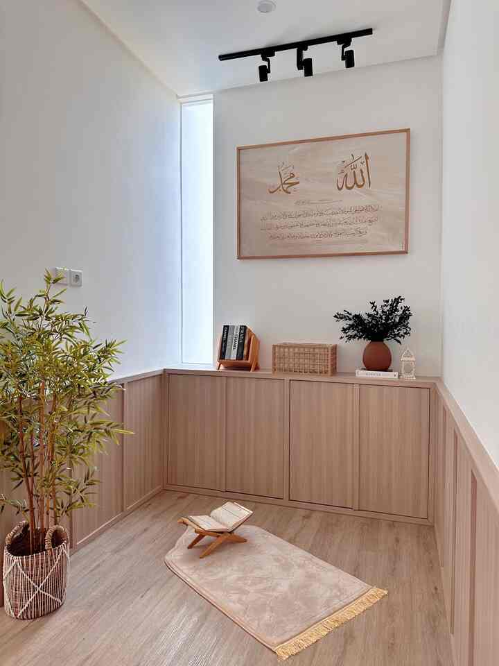 Bright white walls and wood-tone custom cabinets in a compact Japandi-style prayer room with bamboo plant and prayer rug creating a serene atmosphere
