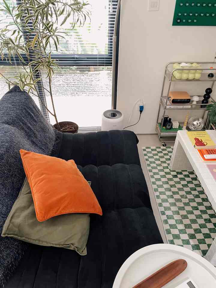 Mid-century modern living room with black sofa, orange cushions, plants by window, and decorative trolley for a cozy atmosphere