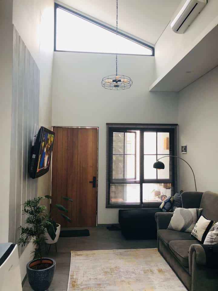 White and gray toned living room with high ceiling, sofa, and plants creating a modern cozy atmosphere