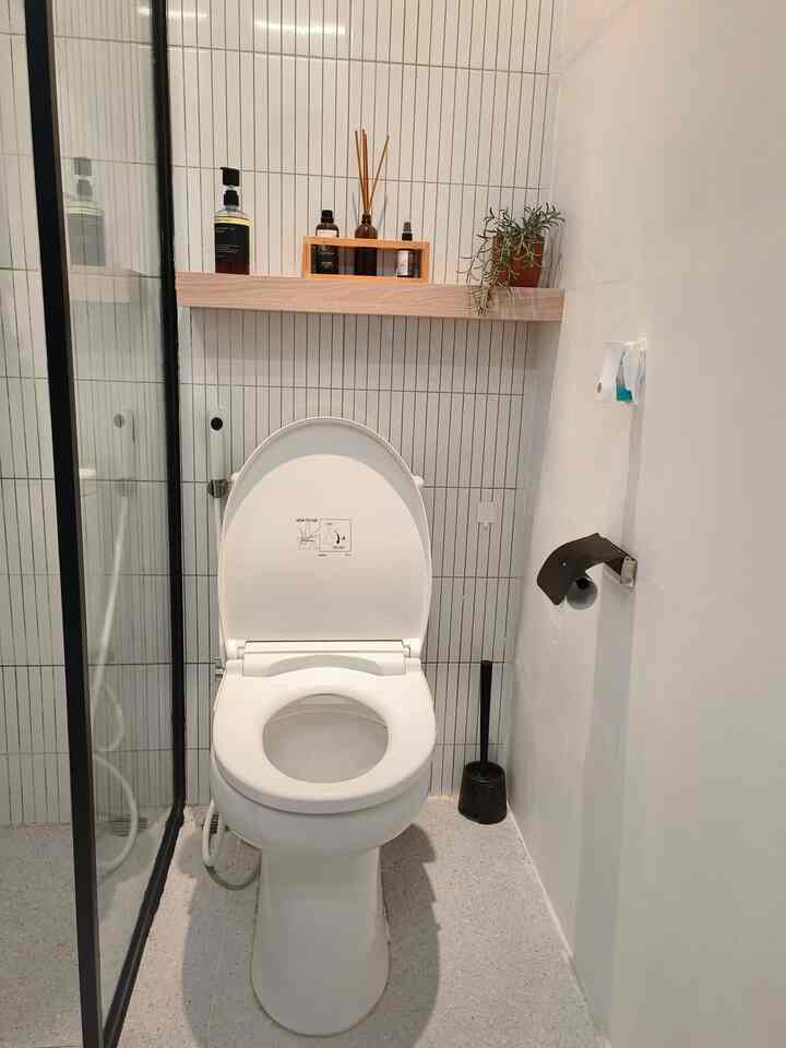 White and light gray toned bathroom featuring a central toilet with custom wooden cabinet shelf holding toiletries, creating a clean look