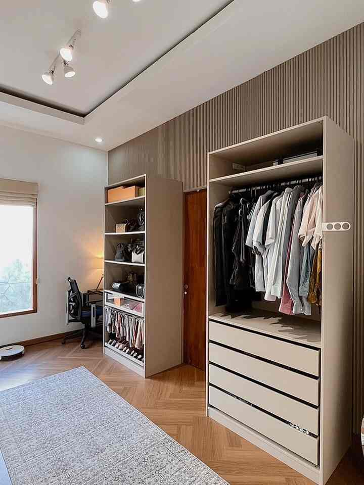 Beige-toned custom walk-in closet featuring wood-tone flooring and a custom-sized carpet creating a clean and organized closet space