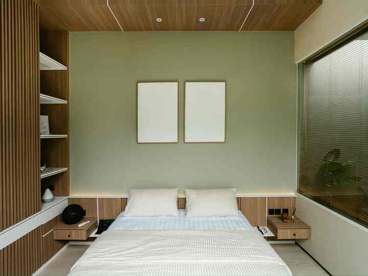 A modern bedroom in beige and wood tones with a centrally placed bed and two minimalist framed artworks on the wall