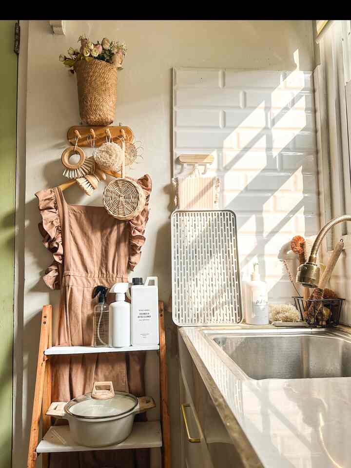 Small kitchen space with natural tones and white tiles, featuring wooden shelving and a linen apron, creating a cozy and organized atmosphere