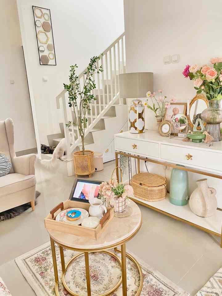 Bright beige and gold toned living room featuring an armchair, round marble table, vases, and plant stand in a shabby chic style