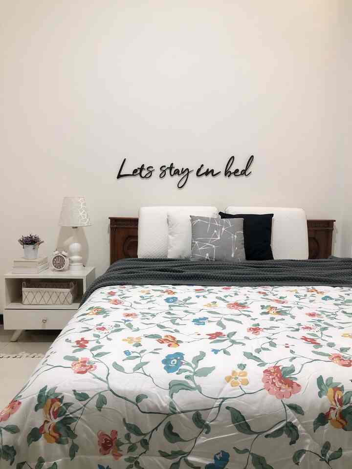 White and gray toned bedroom featuring a white bed with cushions, nightstand, and floral duvet cover, conveying a neat and cozy atmosphere