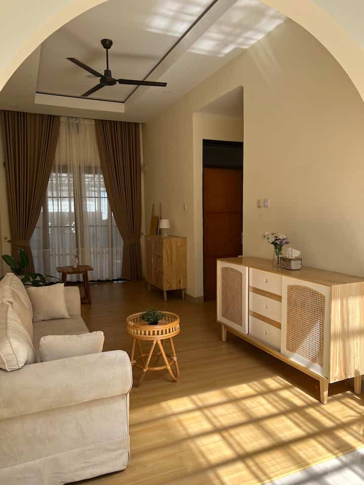 Wood tone and white long narrow living room featuring sofa and console tables with warm, cozy Japandi style ambiance