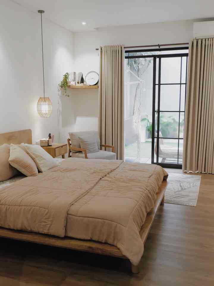 Beige and wood tone bedroom featuring bed, armchair, curtains, and balcony access with cozy natural atmosphere