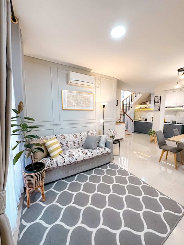 A white and gray tone living room featuring a patterned sofa and carpet, dining table and kitchen integrated in a modern open space layout