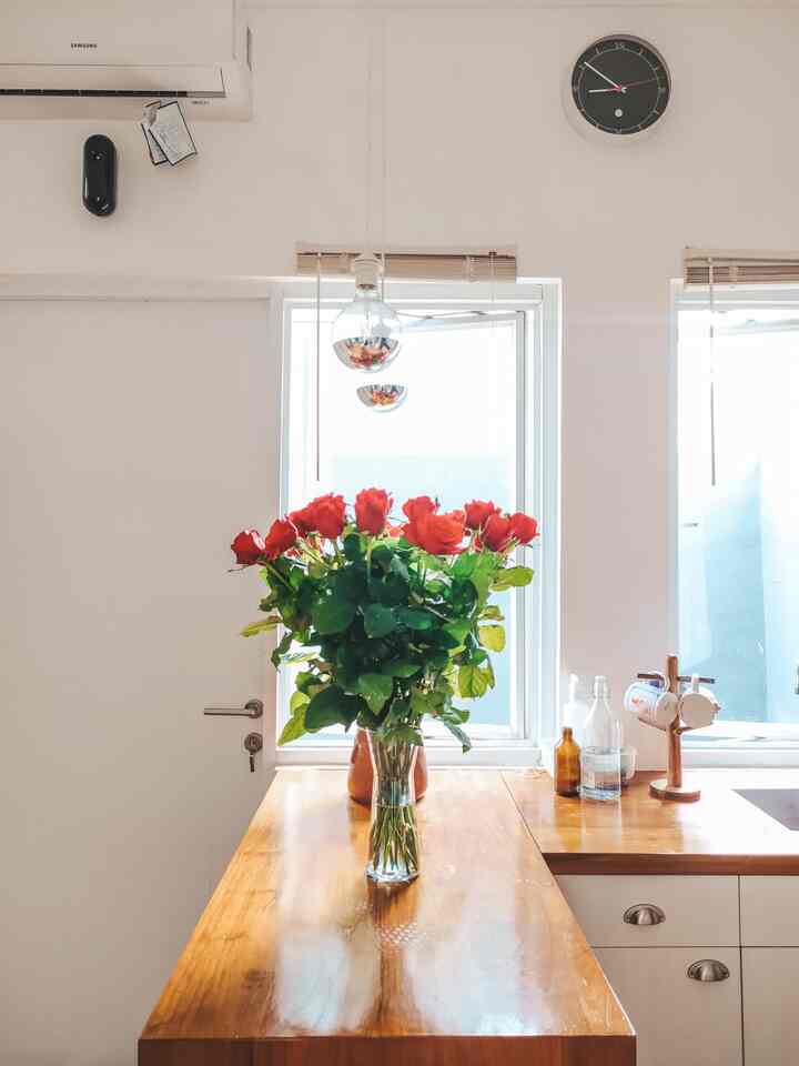 Natural-tone kitchen featuring a wooden countertop with a vibrant red rose vase centerpiece, bright and clean interior
