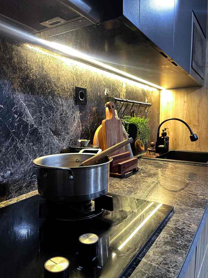 Black and brown toned compact kitchen featuring built-in 2-burner induction stove and wooden cooking utensils