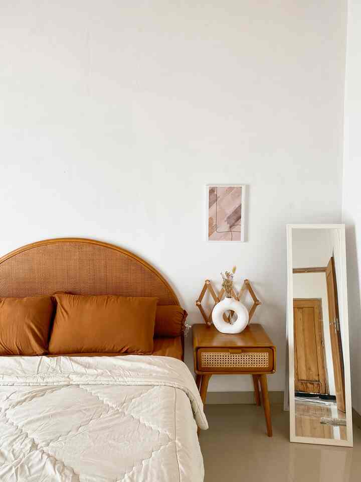 Natural bohemian bedroom with white walls, wood tone bed frame, and side table featuring rattan elements