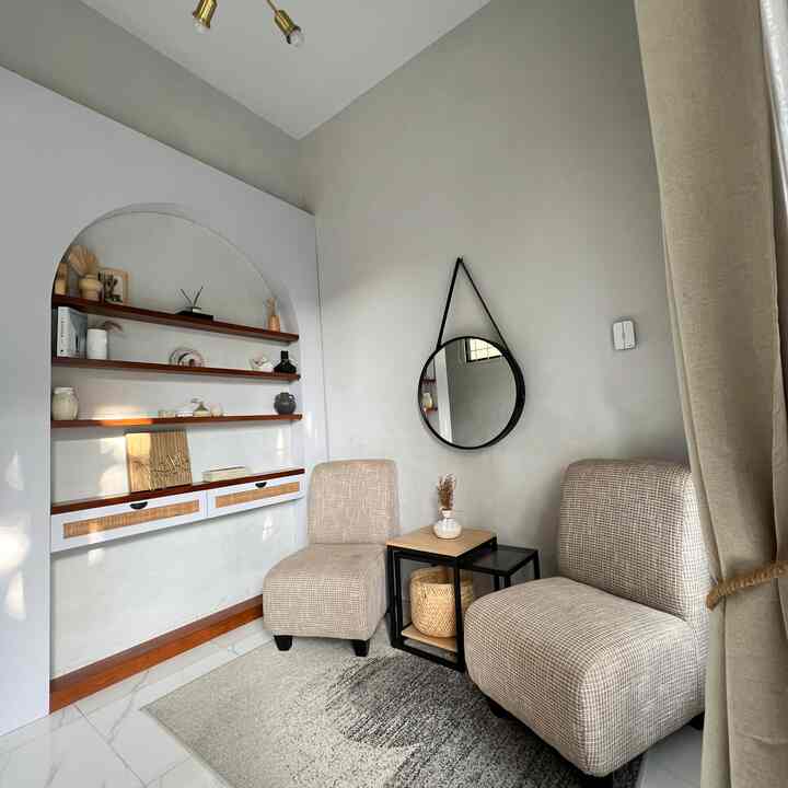 A beige natural-toned small living room featuring two armchairs, a side table, and a round wall mirror creating a cozy atmosphere