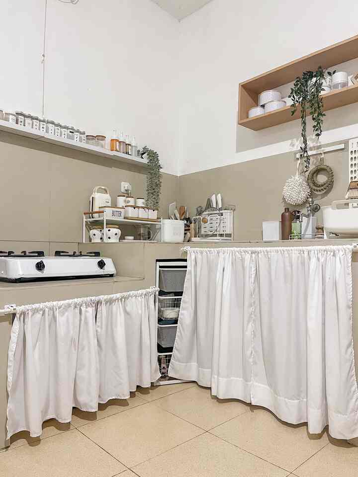 Beige and white-toned kitchen featuring corner storage concealed by curtain panels, creating a neat and cozy atmosphere
