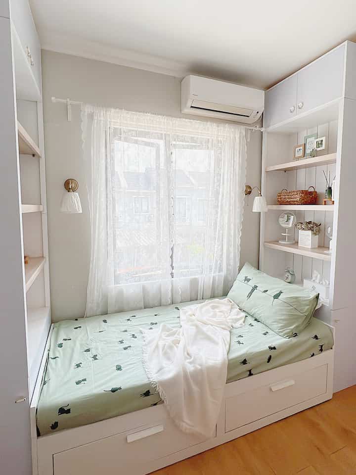 Bright white and natural tone compact kids' bedroom featuring a custom bed frame, sheer curtains, and wall sconces creating a cozy atmosphere