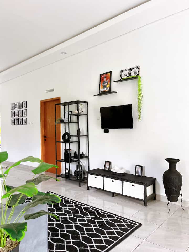 Simple monotone living room with white walls, black furniture, TV, and a black-and-white patterned carpet