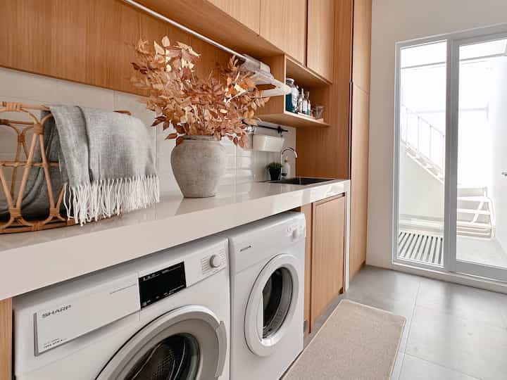 Natural wood tone and white long narrow laundry room featuring multiple cabinets and bright natural light, a practical and clean space