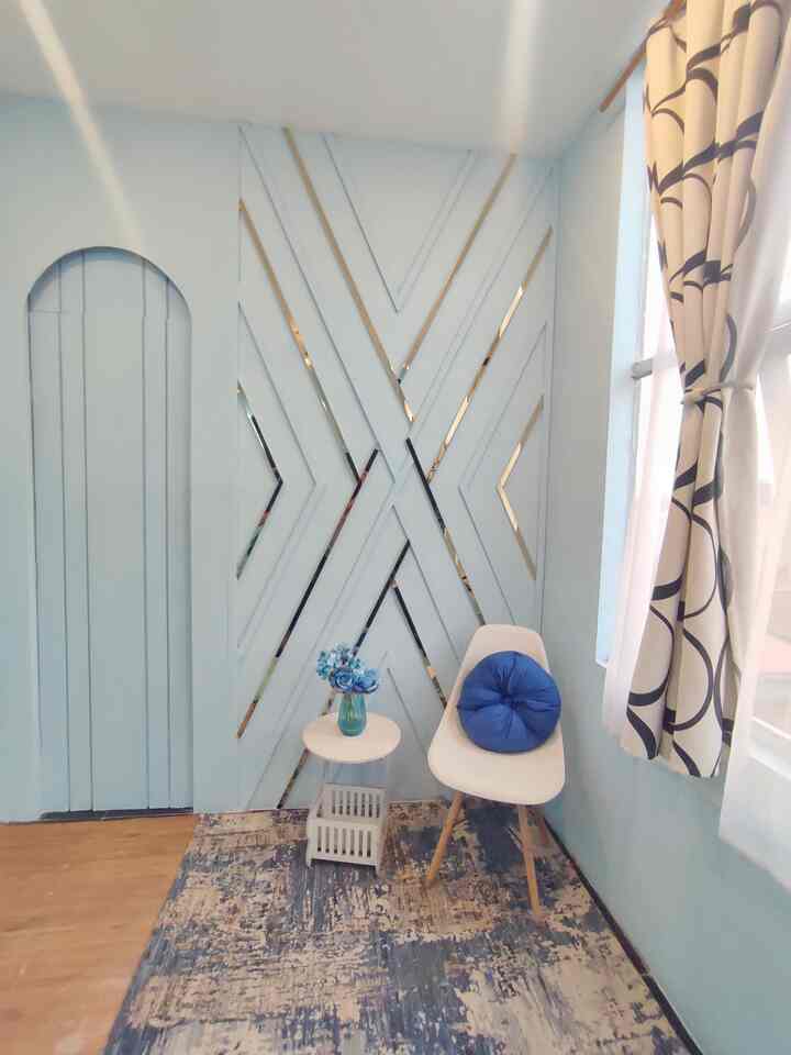 Soft blue tone corner room with gold accents, featuring a simple chair, small table, patterned curtains creating a cozy small space